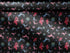 Christmas wrapping paper with a black background featuring colorful, stylized reindeer and Santa's sleigh designs. The reindeer and sleigh silhouettes are filled with skeletal patterns in shades of blue, pink, and red. Multicolored snowflakes in various sizes are scattered throughout. The paper has a whimsical, slightly gothic aesthetic that blends traditional holiday imagery with a unique, edgy twist.